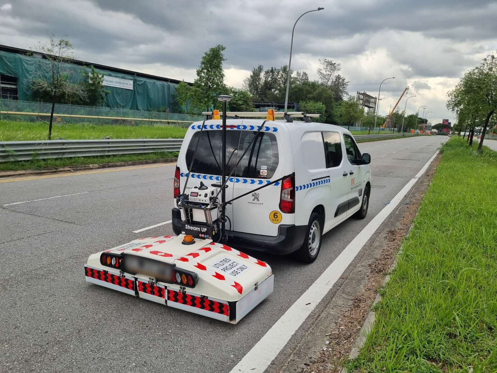 White Peugeot van on a road with equipment attached to the back, likely for utility project use.